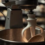 Industrial dough mixer spins with worn wooden spoon leaning against metal frame and warm glow