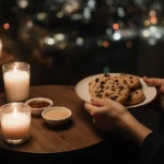 Hands holding Insomnia Cookies with milk and dipping sauces on wooden table near city lights