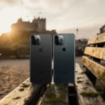 Two smartphones rest side by side on weathered wood with Edinburgh Castle rising behind at sunrise