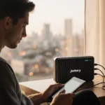 Person charging laptop with Jackery Explorer 300 power station and warm window light showing prepared home setup