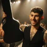Jonas Brothers guitar tech walks backstage with guitar case and confident smile with cheering crowd behind