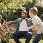Josh Holloway sits on a wooden bench watching his children play with branches and laughter in a green backyard