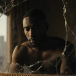 Karamo Brown sits before a cracked mirror with golden light illuminating his face and a blurred cityscape reflected behind
