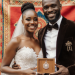 Keely Watson holding wooden box with Akwasidae pendant and engagement ring against vibrant Ghanaian fabric backdrop.