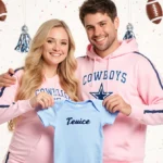 Kelcey and Nate hold a personalized baby onesie with football and pom-pom decorations showing their Dallas Cowboys cheerleade