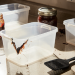 Spatula lying beside cracked plastic container with jam spilling cluttered kitchen and warm light highlighting worn surfaces