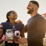 Laila Edwards standing beside Travis Kelce holding a GoFundMe jar with an American flag in background