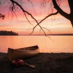 Empty wooden kayak rests on Lake Michigan shoreline with life jacket nearby and sunset reflecting on water