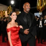 Lauren Hashian and Dwayne Johnson walking the Golden Globes red carpet with golden light illuminating her red gown