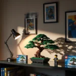 Modern bookshelf holds Lego sets with Bonsai Tree set glowing under warm desk lamp and framed prints on wall
