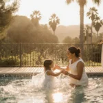 Little girl splashing in pool with grandmother under golden sun with palm trees and Meghan watching nearby