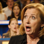 Lisa Ann Walter shouting a curse word on stage with shocked audience faces blurred and golden lighting showing her surprise.