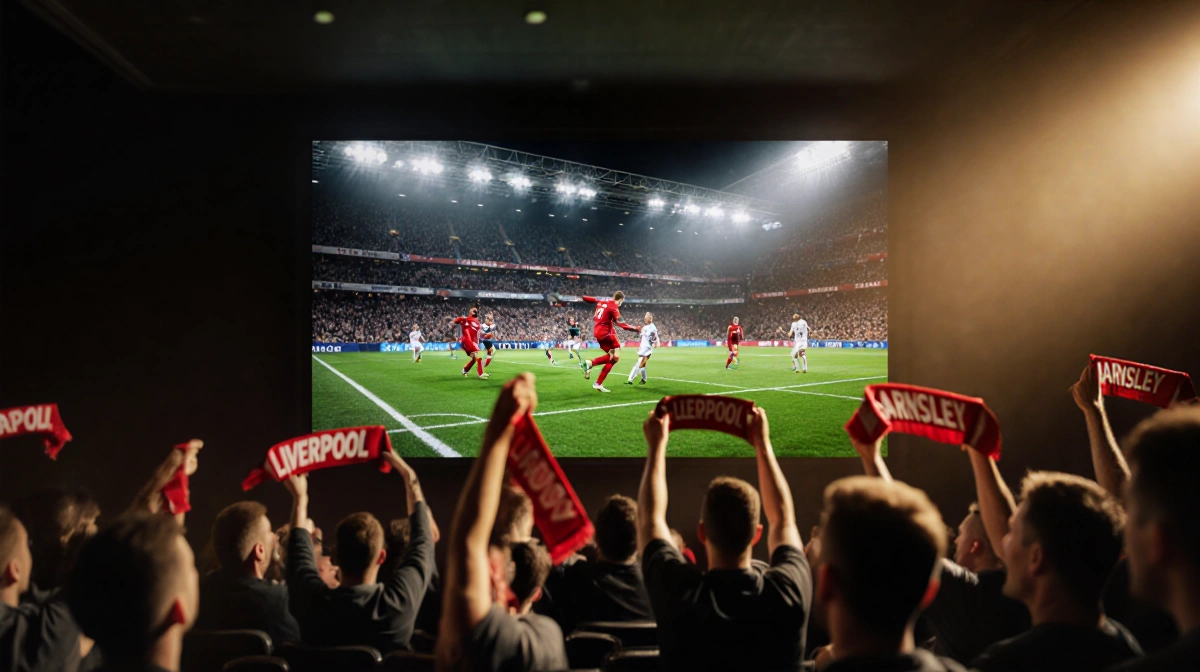 Liverpool fans cheering with scarves raised and stadium TV showing dramatic goal celebration