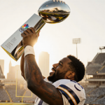 Football player lifts Lombardi Trophy with golden light and blurred stadium seats behind