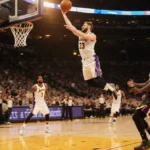 Luka Dončić dunking the basketball with Lakers players cheering under a sunset cityscape