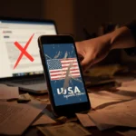 Hand reaching for phone with scratched-off Made in USA logo on cluttered desk with bills and blurred website showing red X