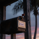 Mailbox standing alone on a weathered porch with a cream envelope marked Autopsy and wispy palm trees casting shadows.