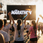 Runners raise arms toward large screen with marathon logo and medals nearby under golden hour light