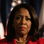 Rep. Marjorie Taylor Greene looking at camera with warm glow and red dress accent on subtle American flag backdrop.
