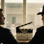 Matt Damon and Clint Eastwood sitting together with film clapboard between them and warm light from windows behind