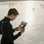 Maxim Naumov stands on ice holding faded photo with parents and tiny skates showing nostalgic figure skating moment