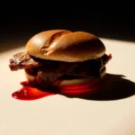 McRib silhouette sits atop white background with faint red glow and discarded pork slice under ominous shadow