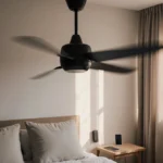 Modern ceiling fan spinning with warm sunlight streaming through window and smart thermostat visible on wall