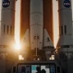 NASA engineer inspecting Space Launch System rocket at dawn with launchpad infrastructure visible behind