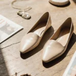 Low-heeled neutral flats rest on worn wood floor with scattered magazines and soft natural light creating chic style
