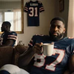 Former NFL player relaxing with coffee and football memorabilia visible in window reflection