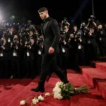 Nick Jonas walking away from Golden Globes with paparazzi flashbulbs and abandoned flowers on steps