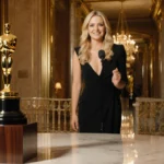 Nikki Glaser presenting at Golden Globes with golden statuettes on pedestal and warm ballroom lighting