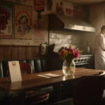 Chef stands at vintage grill with worn wooden booths and faded restaurant signs showing nostalgic charm