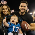 Olivia Culpo and Christian McCaffrey posing with baby daughter wearing Panthers jersey and football at stadium with cheering