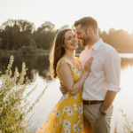 Paige Lorenze smiles with fiancé Tommy Paul at a lake sunset with golden light and blooming flowers showing love.