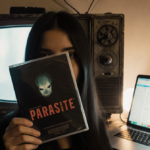 Person holding a Parasite DVD with old TV and laptop glow illuminating classic cinema