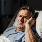 Piers Morgan lying in hospital bed with broken hip and warm lighting showing determination