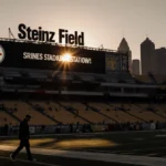 Coach Tomlin walks away from Heinz Field at dusk with empty seats and Pittsburgh skyline glowing behind