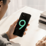 Person holding a Pixel 9 smartphone at an angle with natural light and warm glow on their face over a minimalist desk