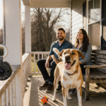 Cozy couple sits on front porch bench with dog Gus wagging tail and ring camera nearby.