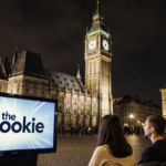 Young adults watching a TV screen with Rookie logo while the Clock tower shines in Prague.