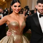 Priyanka Chopra and Nick Jonas walking the red carpet with her gold gown shimmering and his tuxedo gleaming under bright ligh