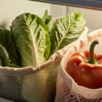 Refrigerator drawer holds fresh romaine lettuce and red peppers in linen bag with wilted lettuce in mesh bag beside discolore