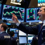 Trader points excitedly at Progyny stock ticker on screen with blue-green trading floor lights and focused investors behind