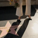 Rachel McAdams smiling holding bouquet with Hollywood Walk of Fame stars and handprints in front and faded couch hinting film