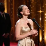 Rachel McAdams standing at microphone at award ceremony with golden lights and a red carpet