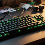 Razer BlackWidow V3 Hyperspeed Mini keyboard glowing with golden light on cluttered desk with gaming cables and accessories