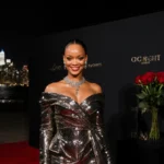 Rihanna smiles confidently on red carpet with metallic outfit glowing under city lights and roses beside her