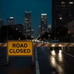 Road closed sign blocks empty Santa Monica Boulevard with wet pavement reflecting city lights and skyscrapers rising behind