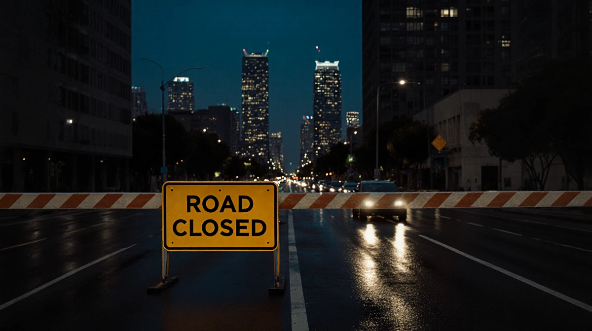 Road closed sign blocks empty Santa Monica Boulevard with wet pavement reflecting city lights and skyscrapers rising behind
